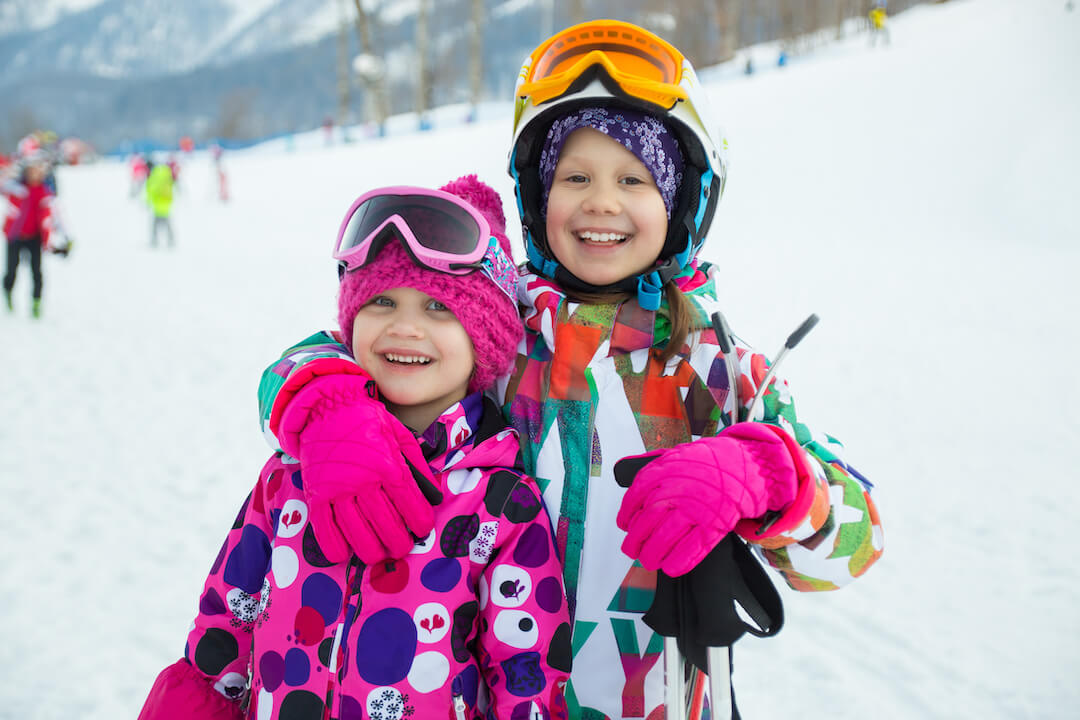 Two kids smiling in all of their ski gear.