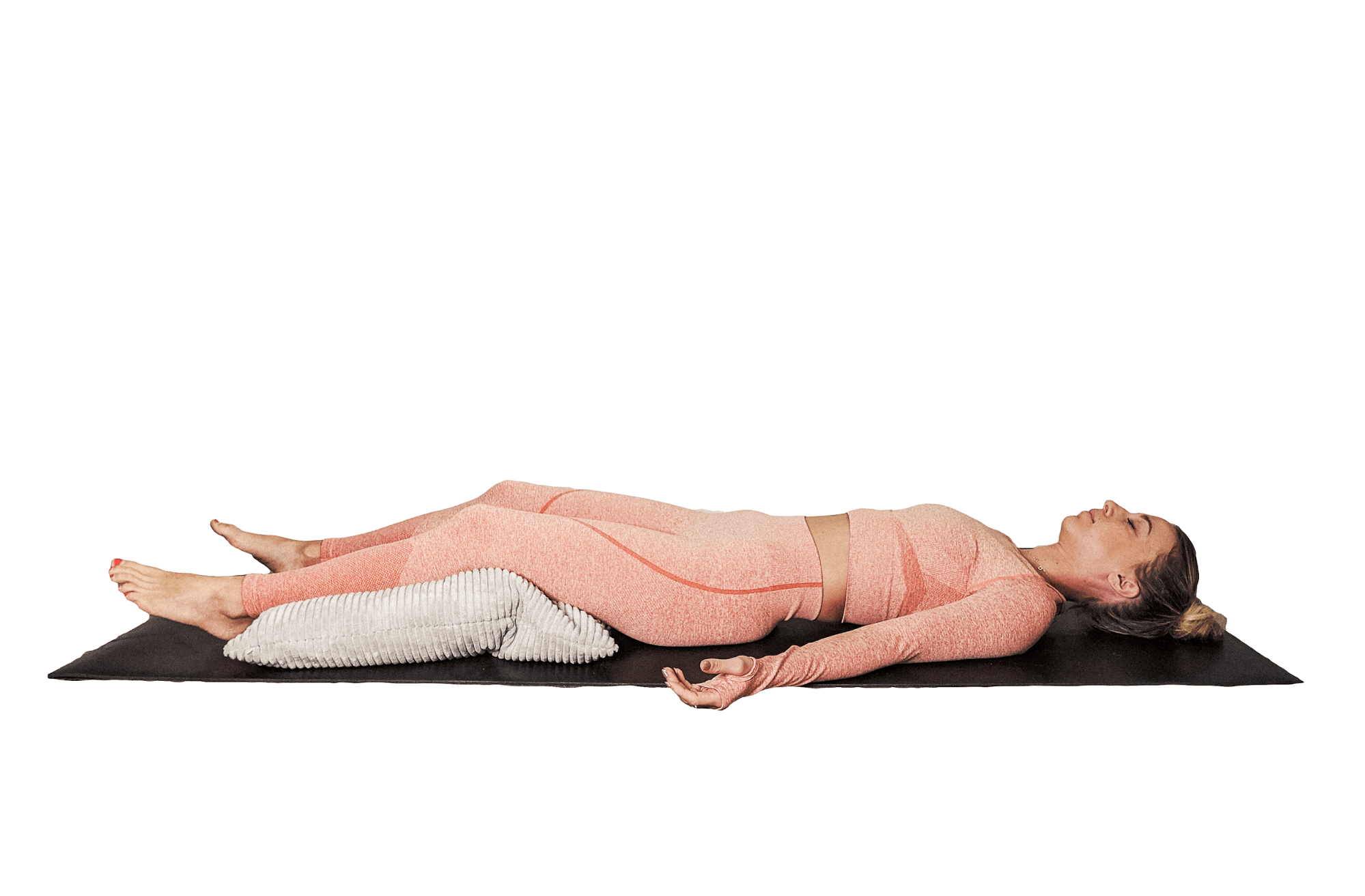 SUPPORTED SAVASANA. Lie on your back with a pillow resting underneath your knees and your arms comfortably by your sides.