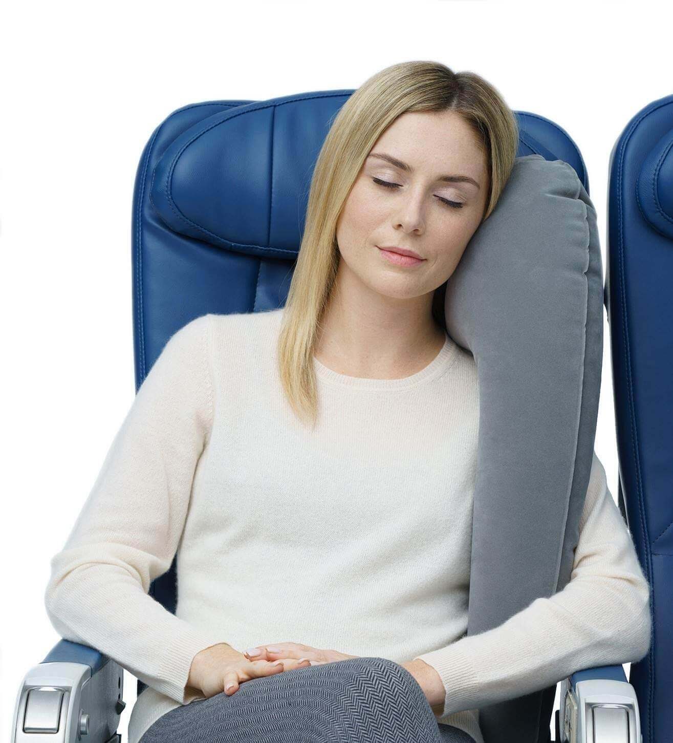 A woman sleeping on a plane with a full body pillow.