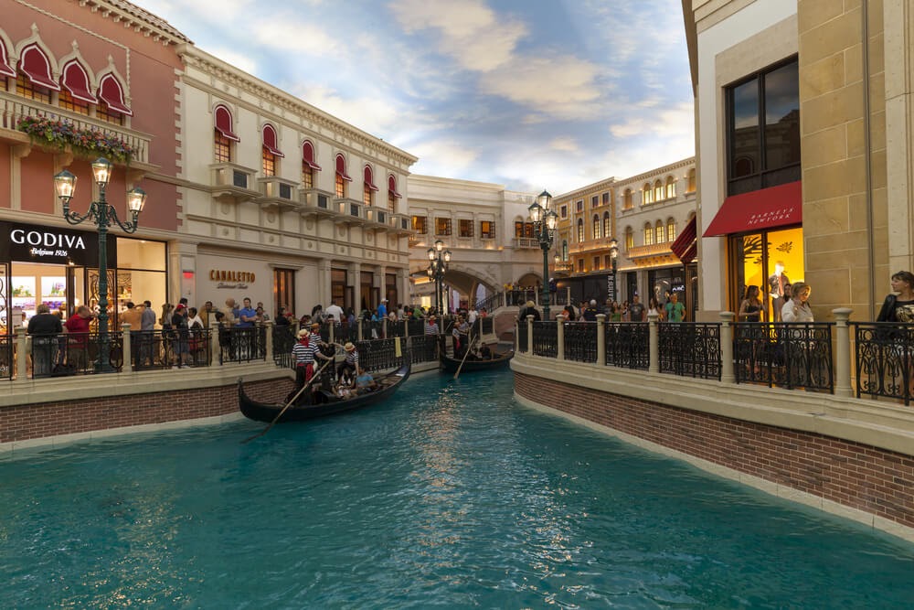 Gondolas float down canal and shoppers pass storefronts