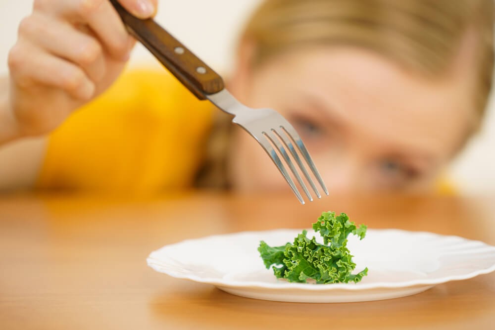 A fork pokes at a small piece of greenery on plate