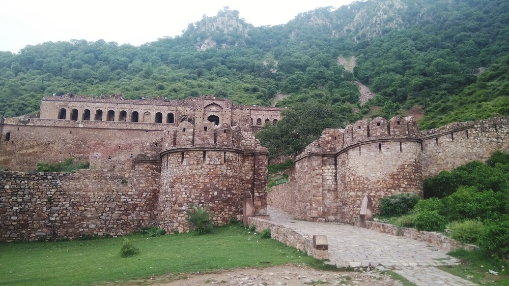Bhangarh Fort in India. Stone building set into green hillside.