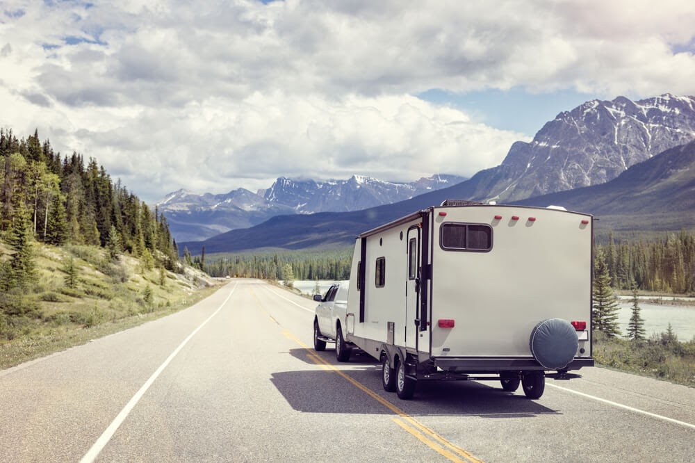 RV driving down the highway with the mountains and a river beside them.