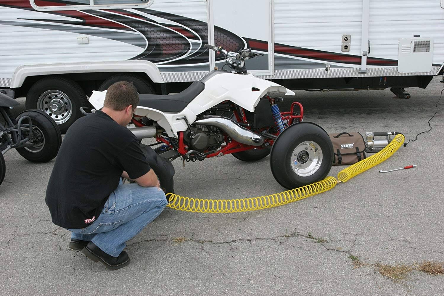 Person in front of an RV putting air into the tires of a white ATV
