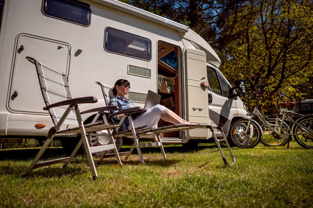 Woman in front of RV sitting in a camp chair working on a laptop.