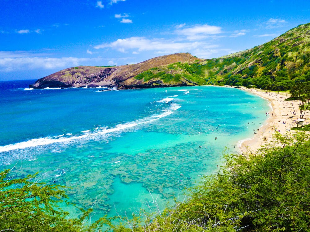 Tropical bay with white sand beach and reef. Photo shows blue water and blue sky and green hills.