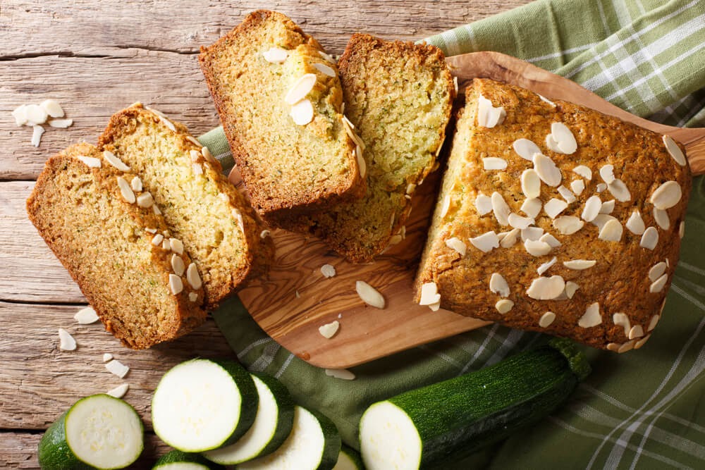 Loaf of zucchini bread with nuts. A sliced zucchini sits next to the sliced loaf.