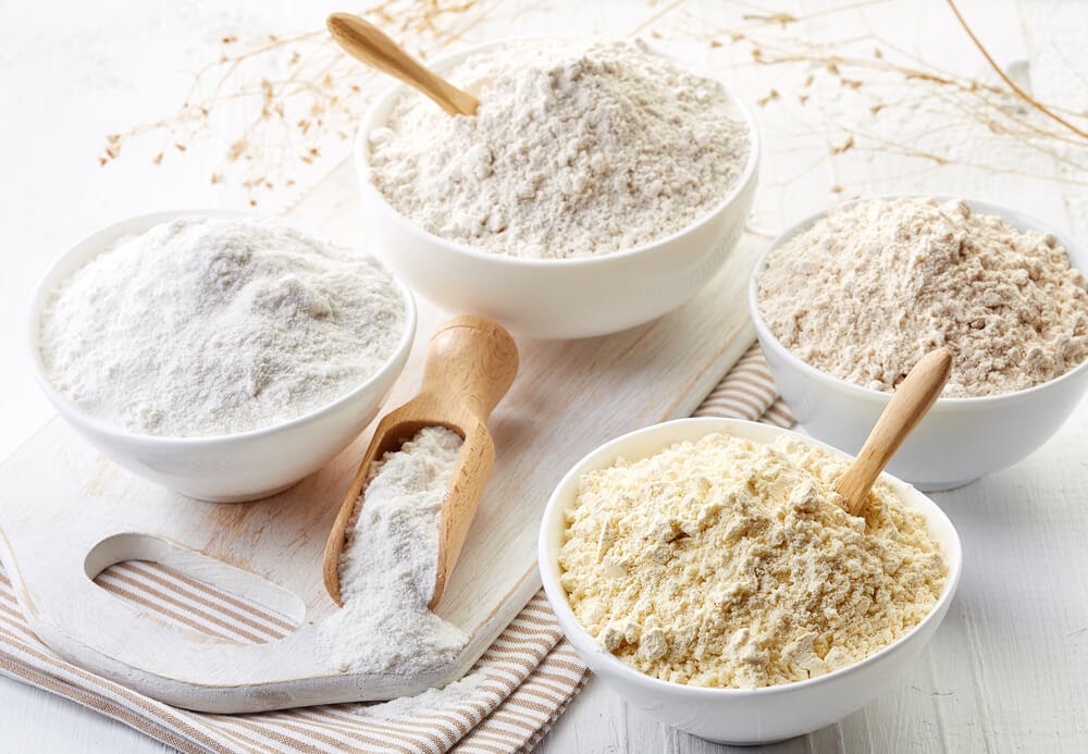Four bowls of different flour with wooden spoons in them.