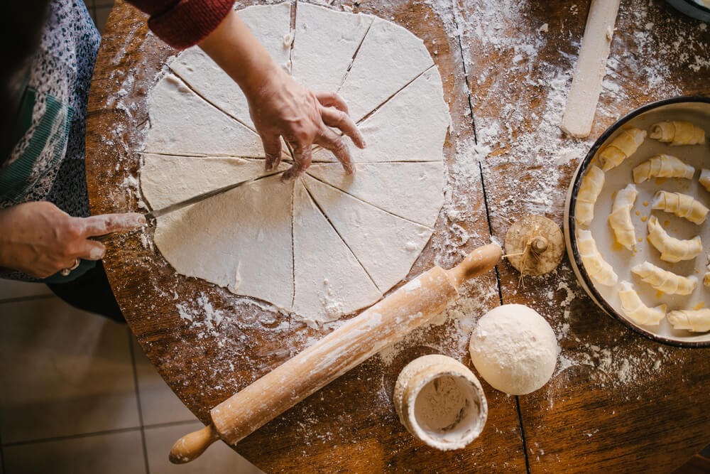 Overhead shot of person working with dough on a board. A round piece has been thinly rolled and is cut into pie shaped pieces.