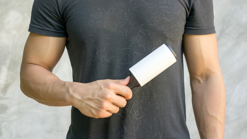 Man wearing black shirt covered in animal fur. He is holding a sticky lint roller.