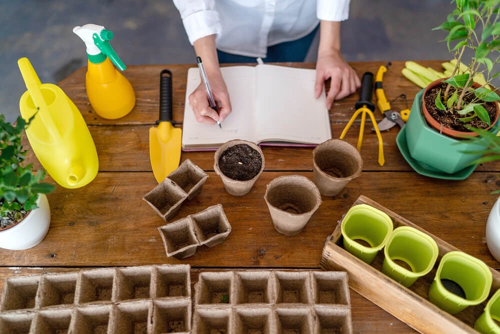 Garden table with pots and potting supplies. Hands are writing in a book.