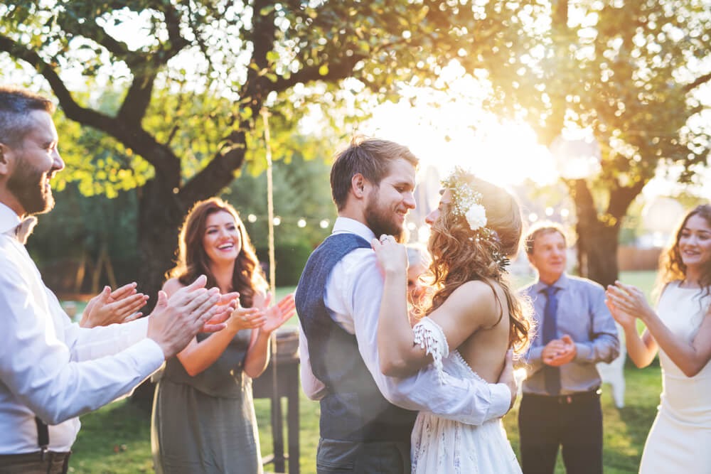Couple dancing in wedding attire. The sun is shining and everyone is smiling
