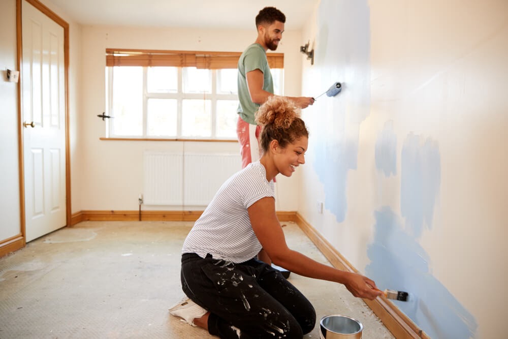 Man and woman painting a yellow room blue.