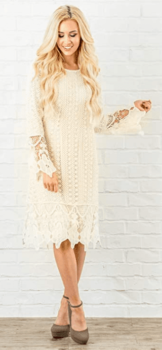 White crochet dress on blonde model standing in front on a white brick wall.