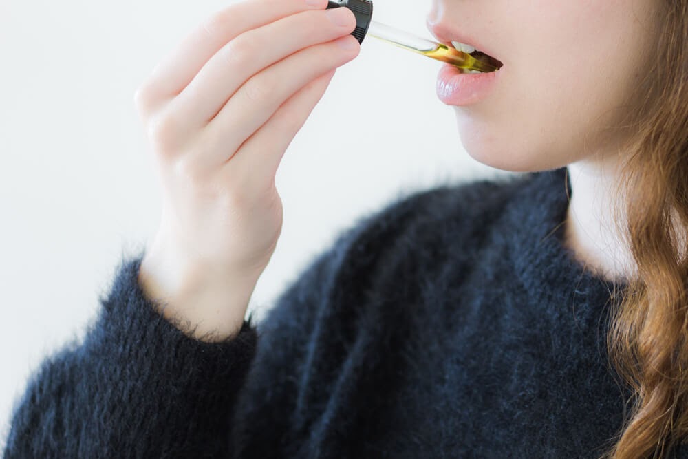 Woman putting tincture under her tongue.