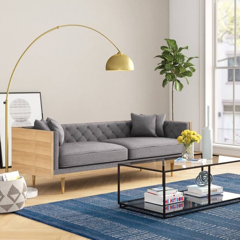 Sun filled living room with grey couch and gold curved lamp.