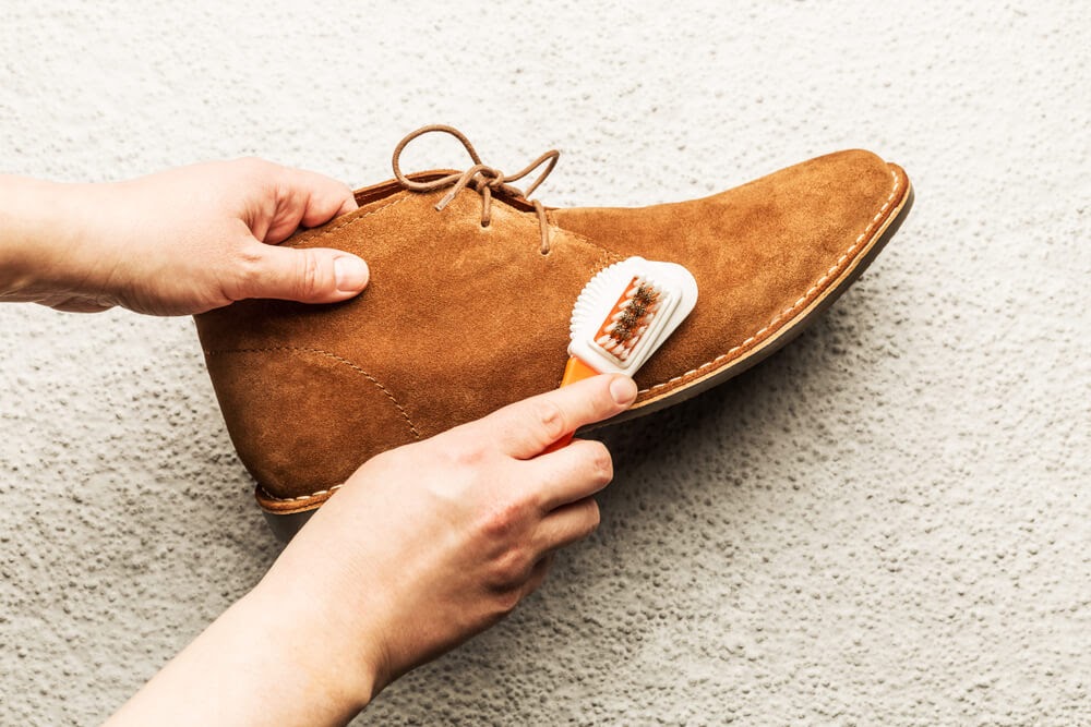 Person cleaning brown suede shoes with a brush.