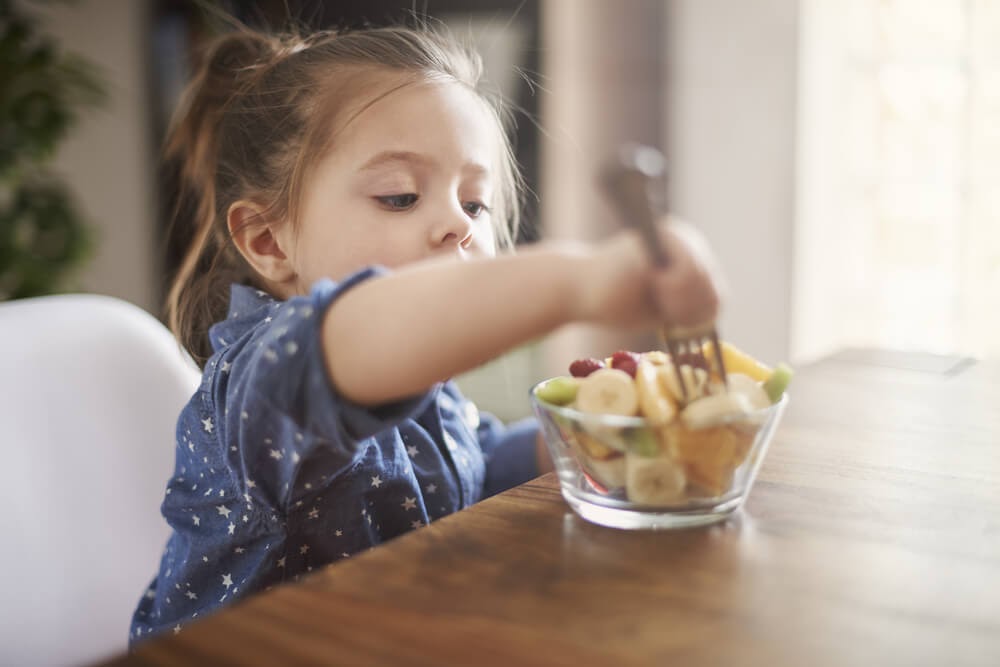 Small girl eating a bowl of cut fruit.