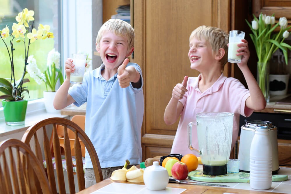 Two young children give a thumbs up while drinking smoothies.