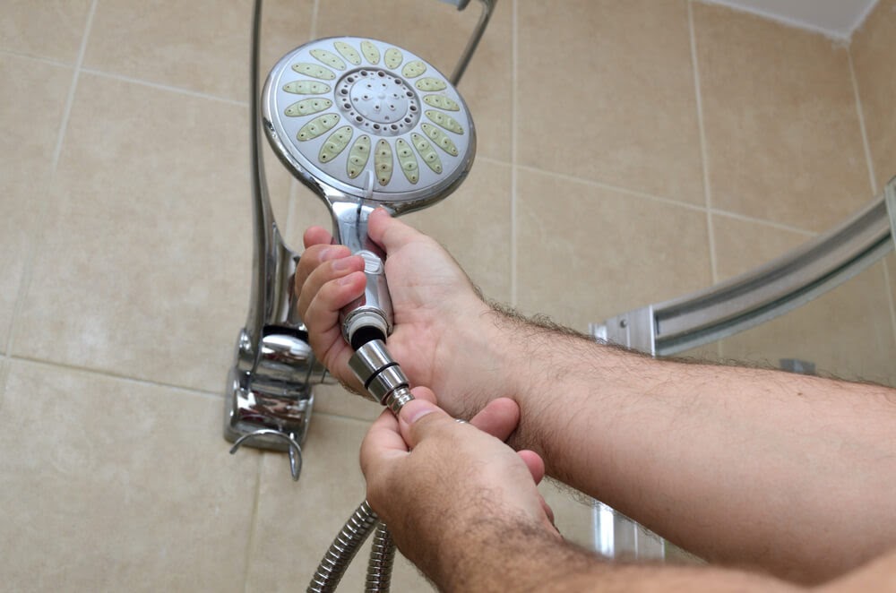 Man holding up shower head in tiled shower