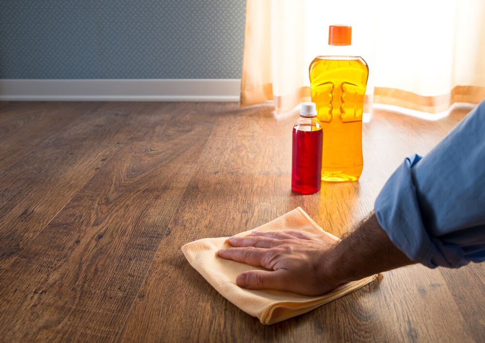 Man wiping down hardwood floor with cleaners in the background