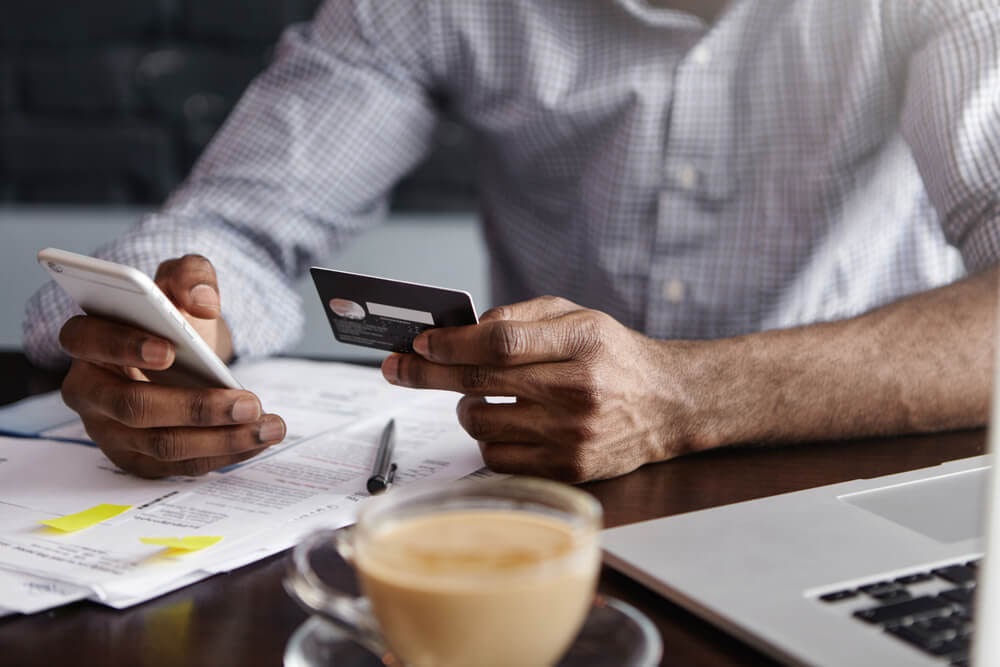 Man holding credit card and phone. He appears to be making a payment of some kind.