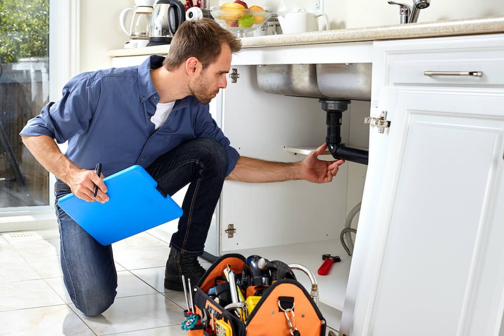 Man looking at the plumbing under the sink.