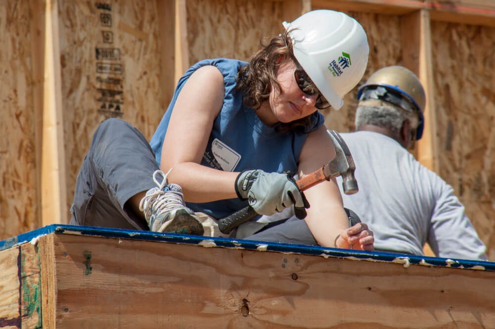 Woman working on a building with her Habitat for Humanity hat on