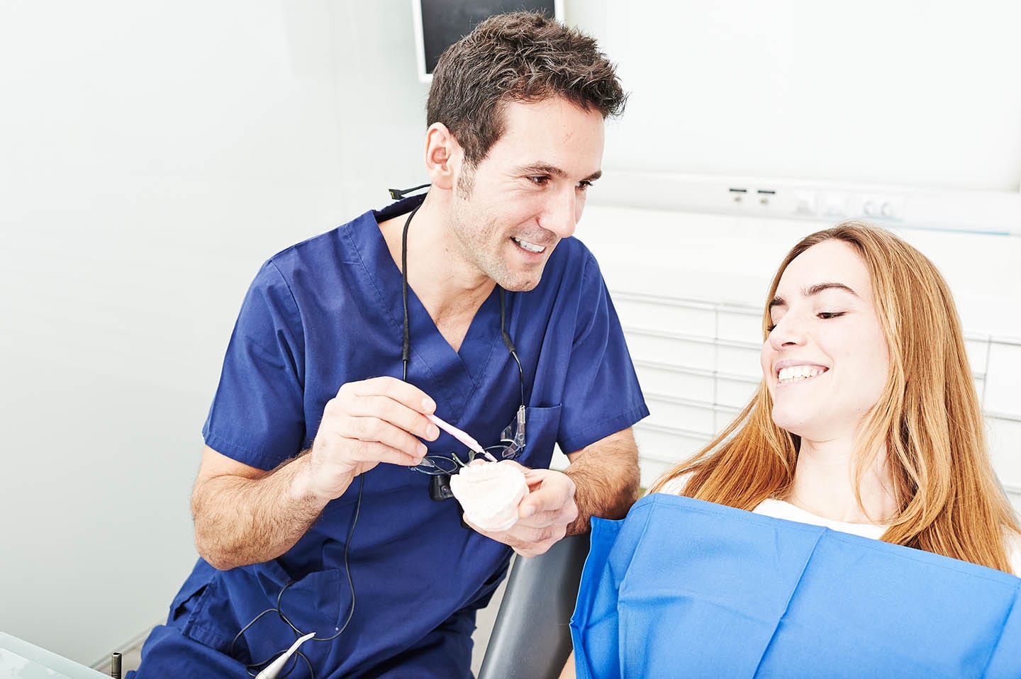 doctor showing a woman patient something on a clay teeth mold