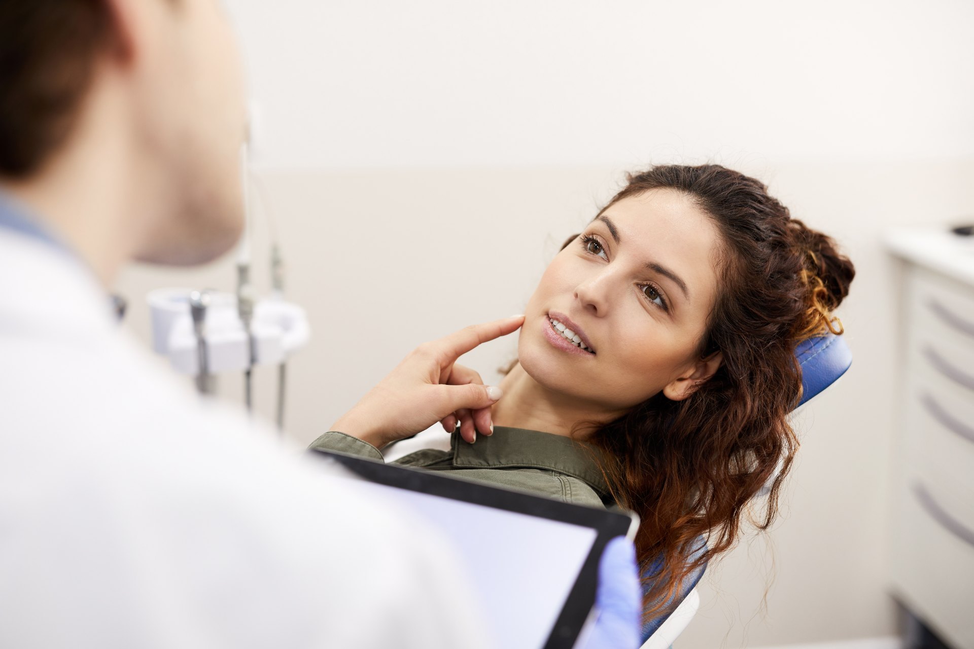 a woman patient pointing to the right side of her face as the dentist examines her