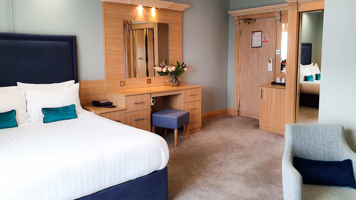 Double bed in Bournemouth hotel bedroom with room phone, vanity, stool and flowers in background