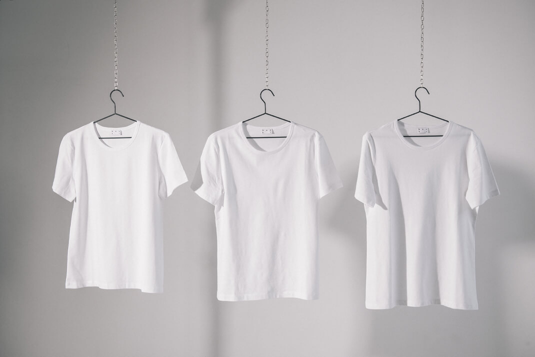 Three white Asket Tee Shirts hanging up to show varying lengths available