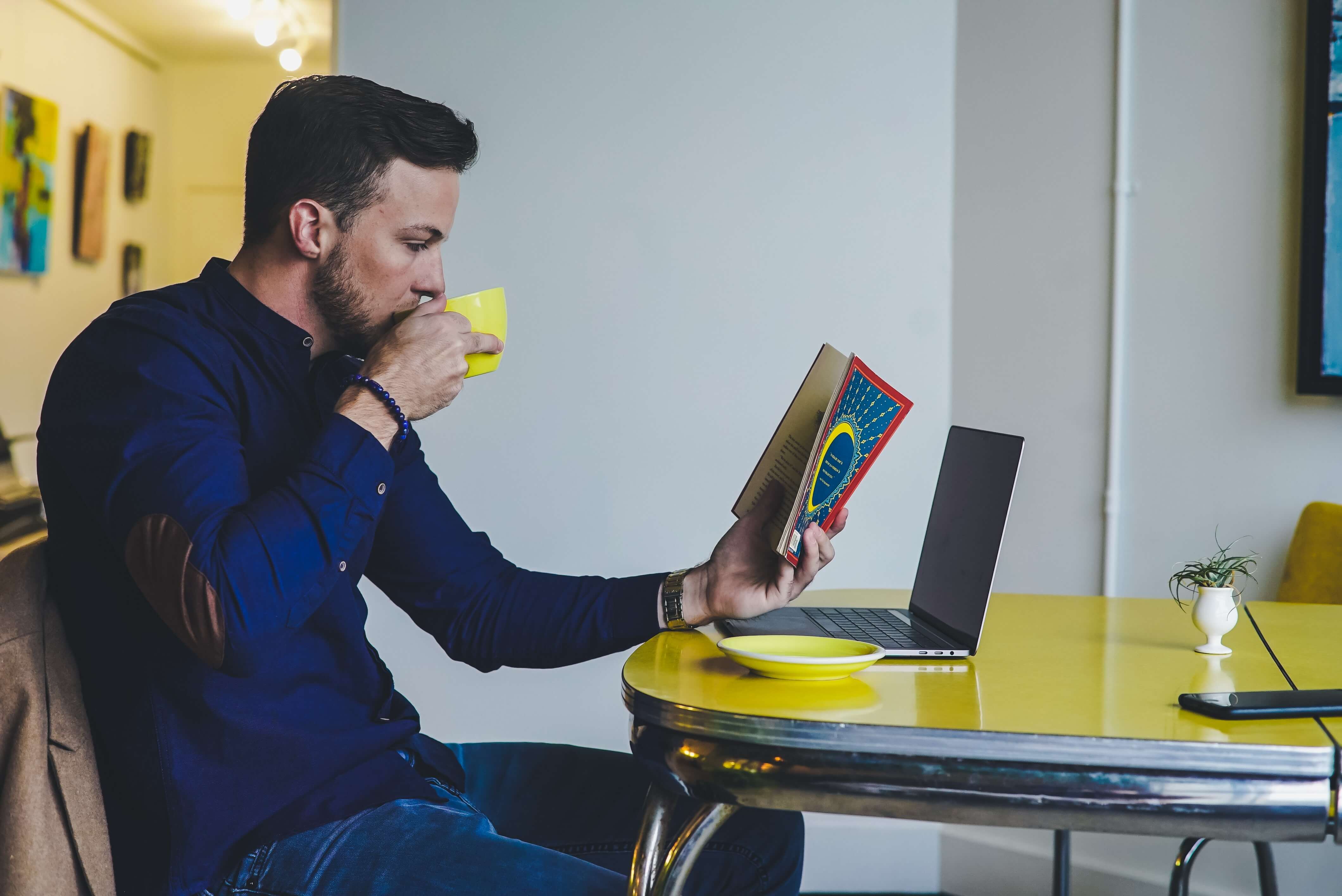 Man drinks coffee at a table while reading about heutagogy and self-managed learning