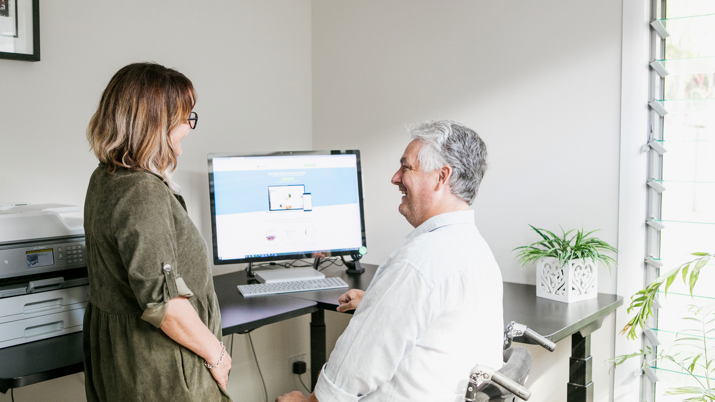 A man and woman looking at a computer in their office