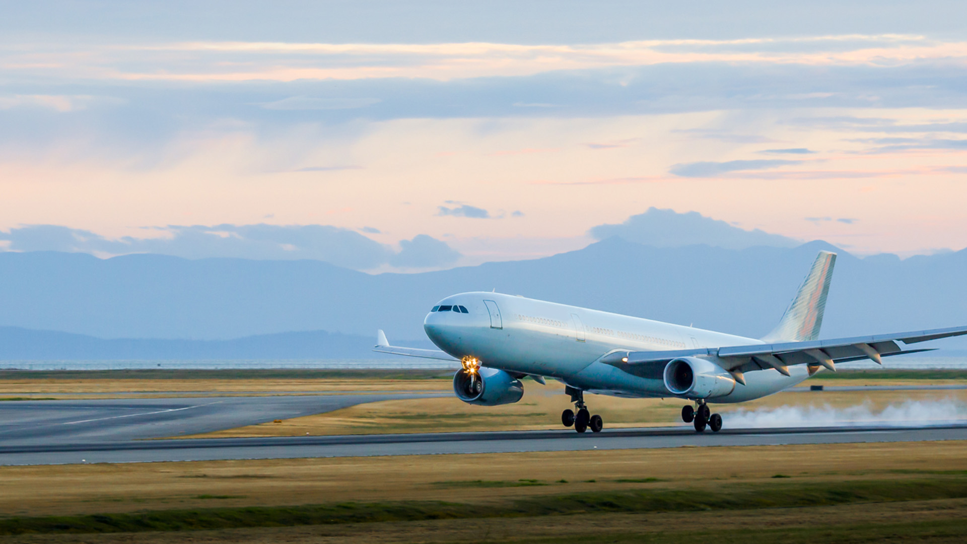 A plane landing with a sunset behind it.