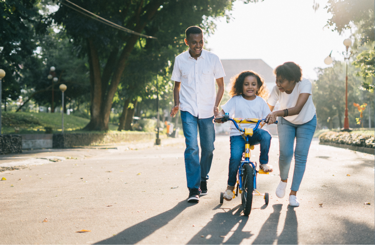 Parents helping child learn to ride a bike