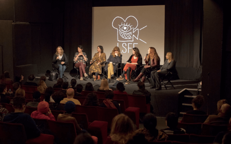 people sitting on chairs on stage on a panel in front of audience
