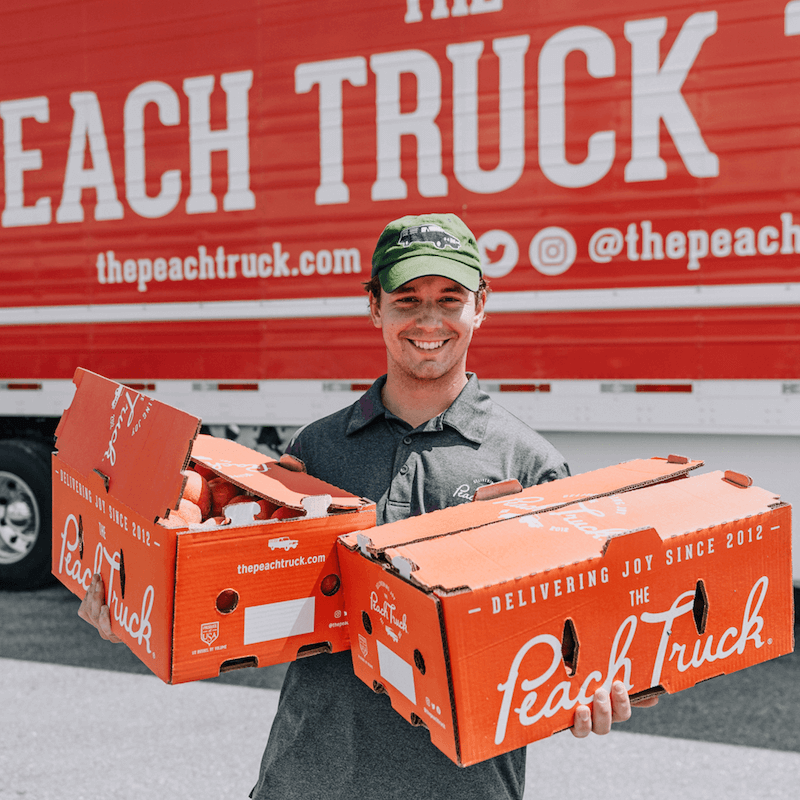 Man holding boxes of peaches in front of the Peach Truck