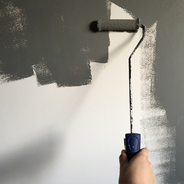 person roller painting their wall gray using home renovation tips