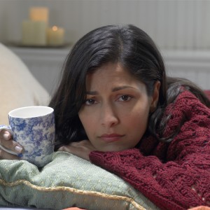 Woman on bed holding cup, resting chin on arm, portrait, close-up