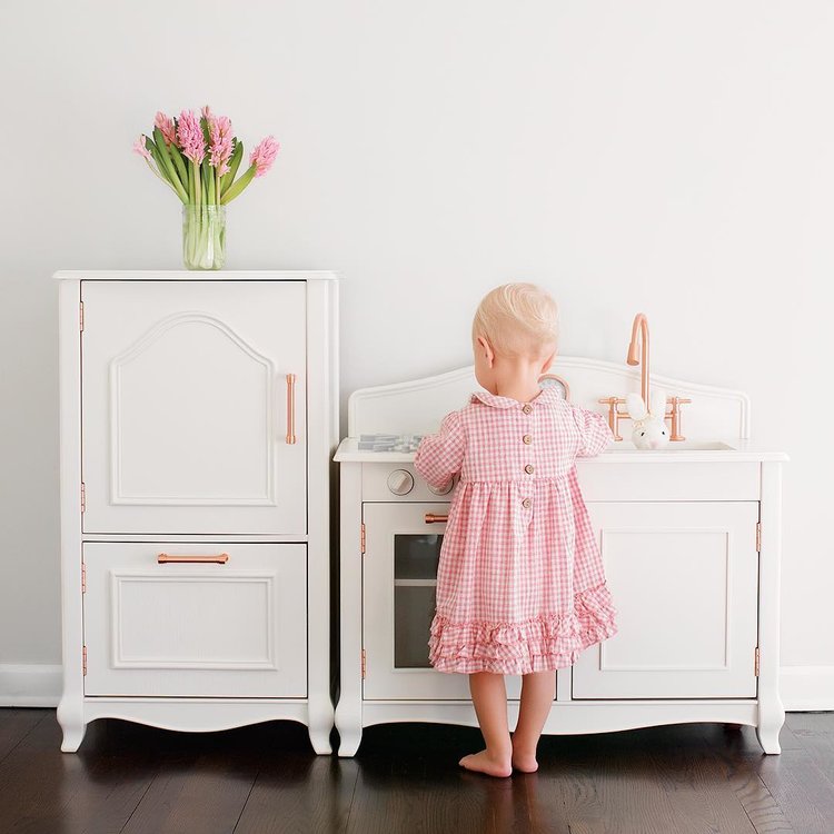 Foto de menina brincando na cozinha de brinquedo com alças de cobre e flores.