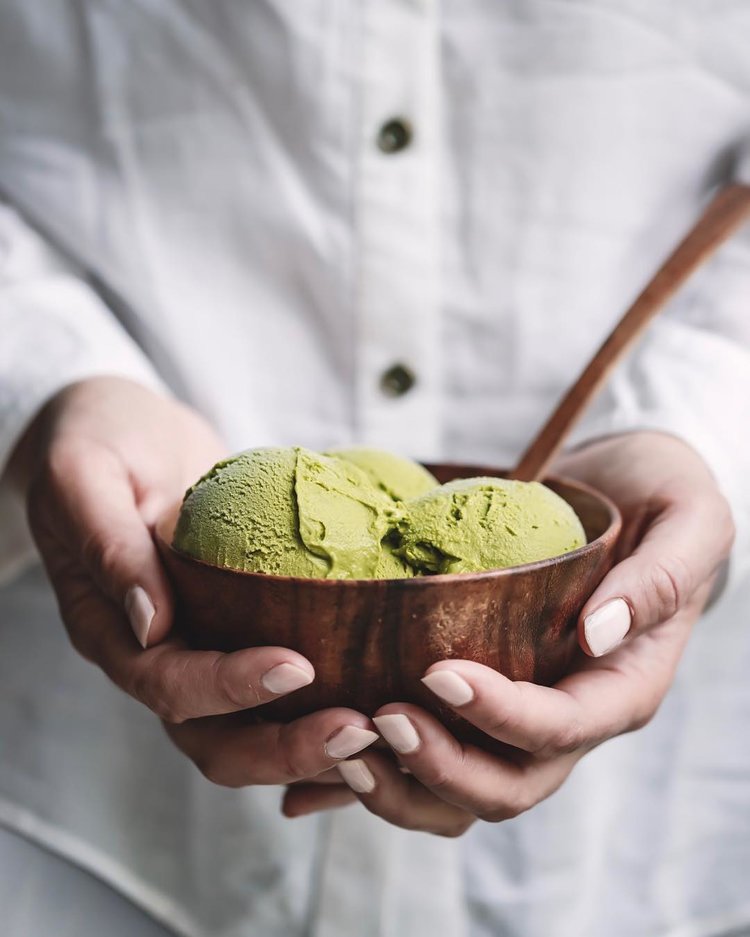 Mãos segurando um sorvete matcha em uma tigela de madeira rústica