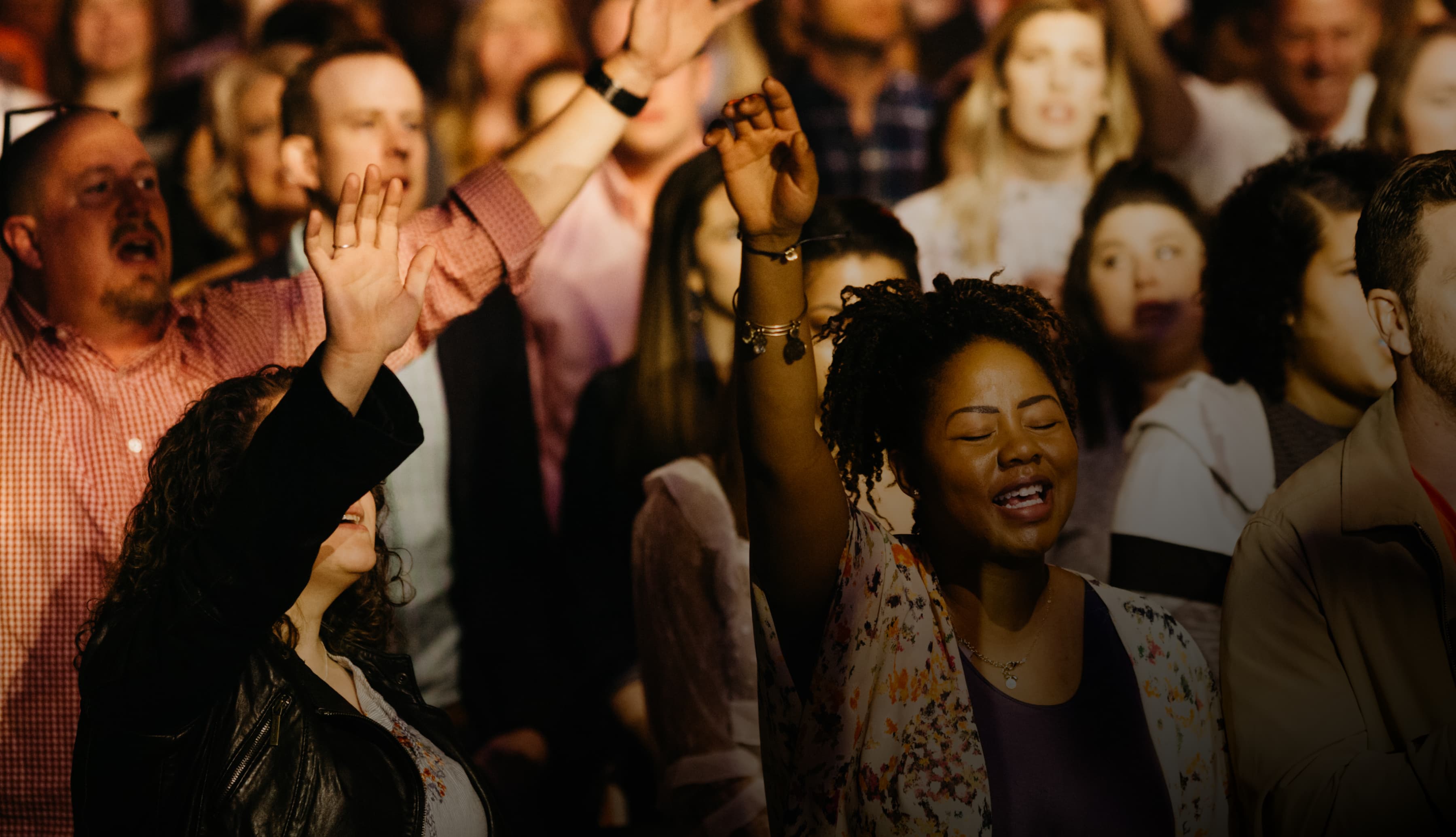 A crowd of worshippers lift their hands in praise.