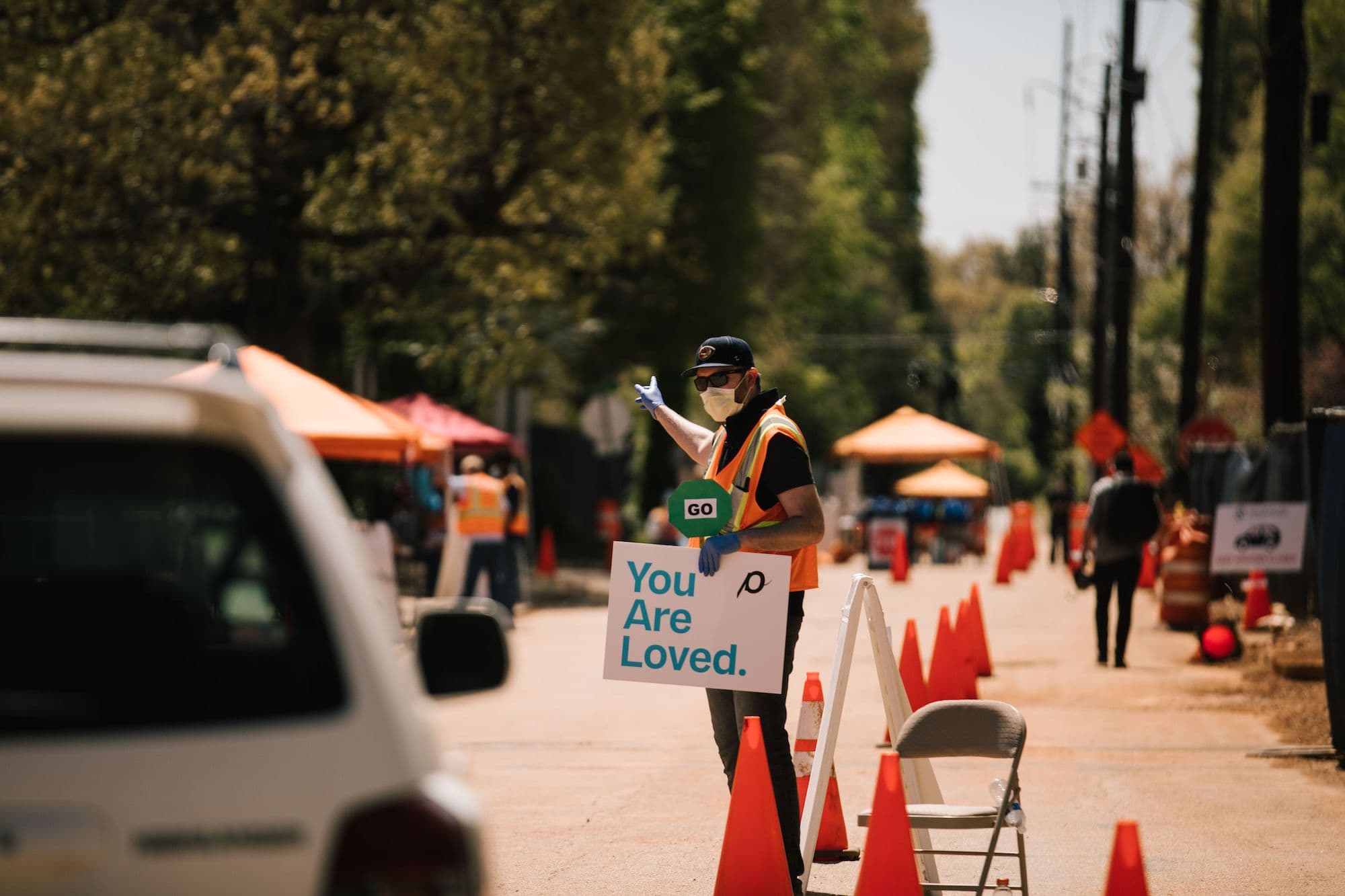 A man directs traffic while holding a sign that says "You are loved".