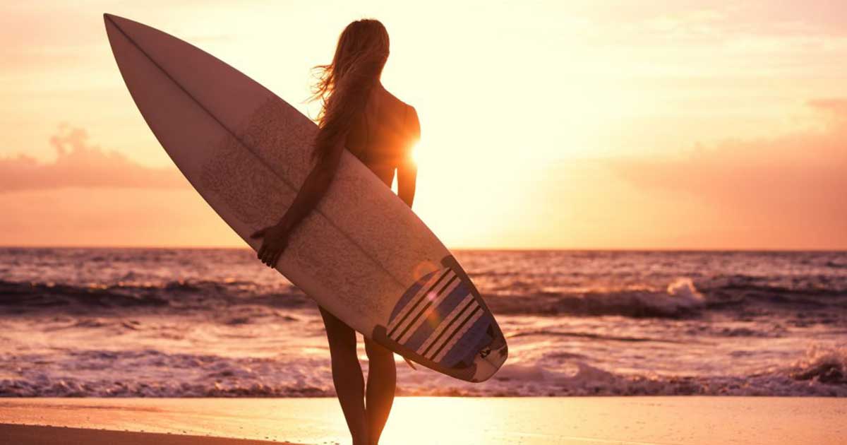 a woman holding a surfboard looking out to sea at sunset