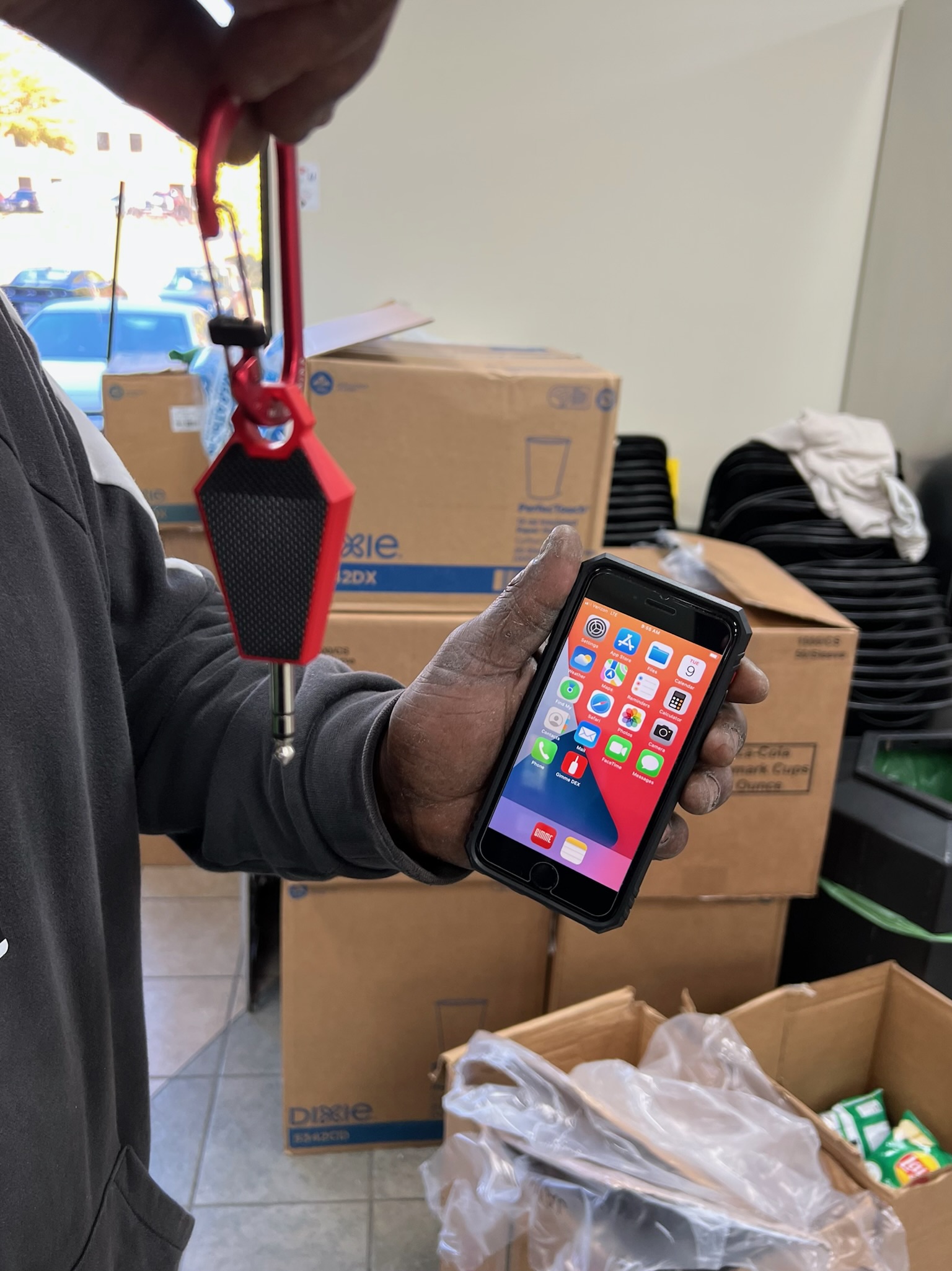 A full service vending or direct store delivery (DSD) route driver holding the wireless Bluetooth (BLE) DEX Gimme Key Pro hardware paired with his iOS iPhone running the Gimme Field app in the field. 