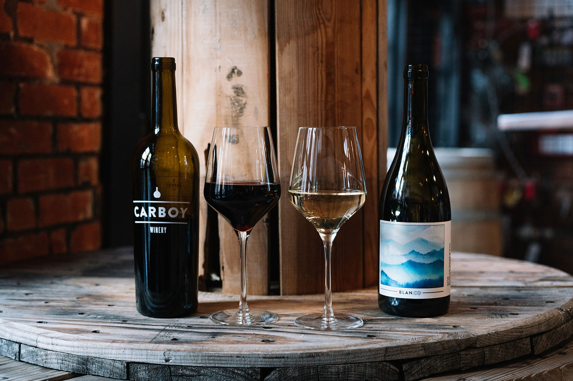 Two bottles of Carboy Winery wine next to two poured glasses of red and white wine.