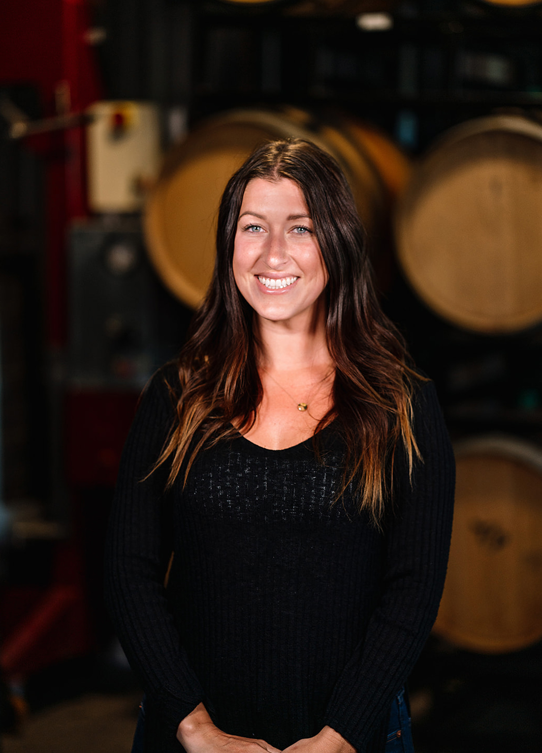 Carboy Events Coordinator, Mallory Eldred, standing in front of wine barrels