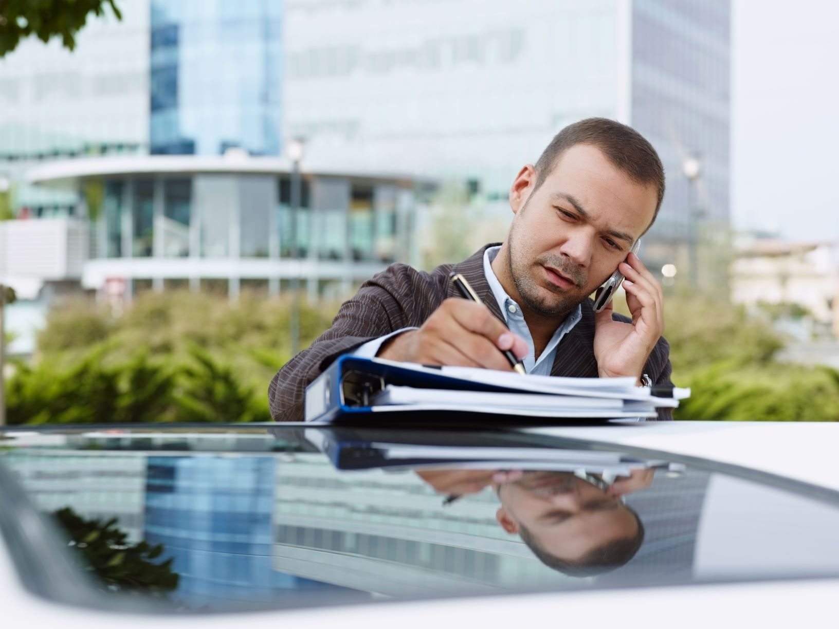 man doing paperwork outside on top of his car