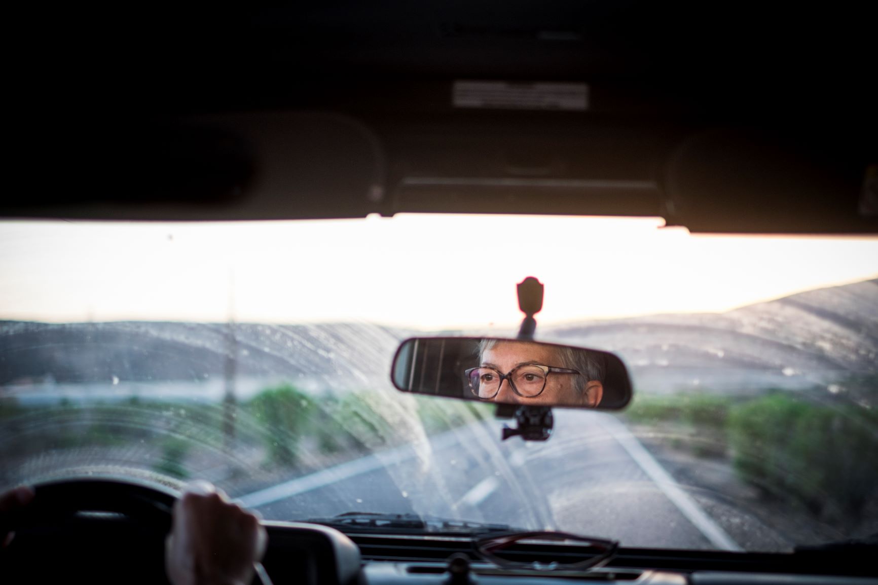 older woman driving on road at sunset